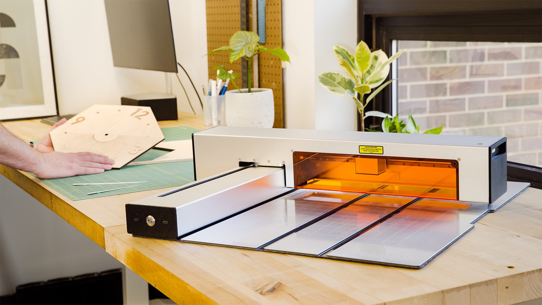 The Optic open on a workbench, orange shield glowing, beside a laser-cut wooden clock face